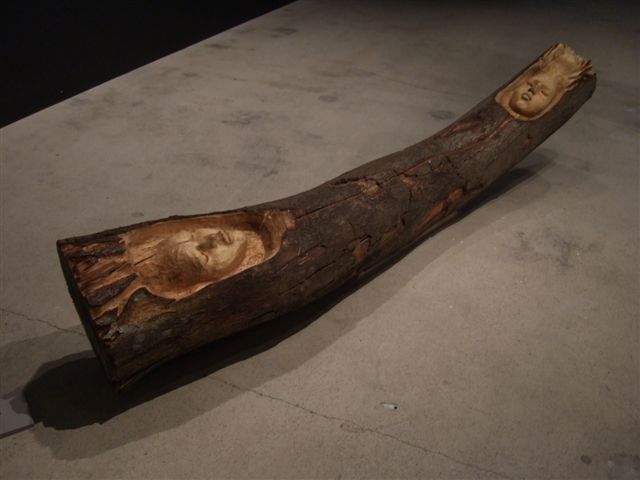 Wooden log sculpture with carved human faces by Sanna Karlsson-Sutisna, from the Iroko exhibition at EMMA – Espoo Museum of Modern Art, 2010.