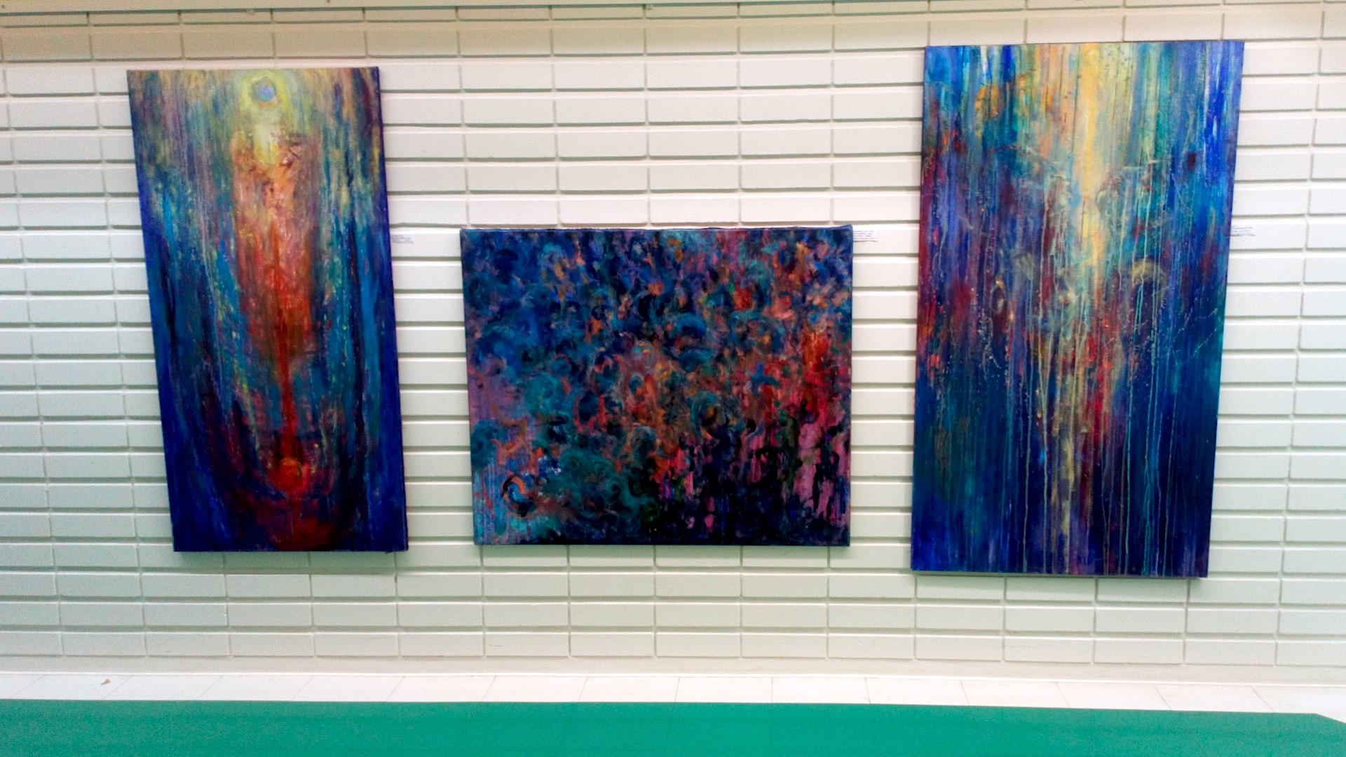 Encounter - Exhibition by Sanna Karlsson-Sutisna - Three blue abstract paintings with flowing vertical forms displayed on a white-tiled corridor wall. - Jorvi hospital 2019.