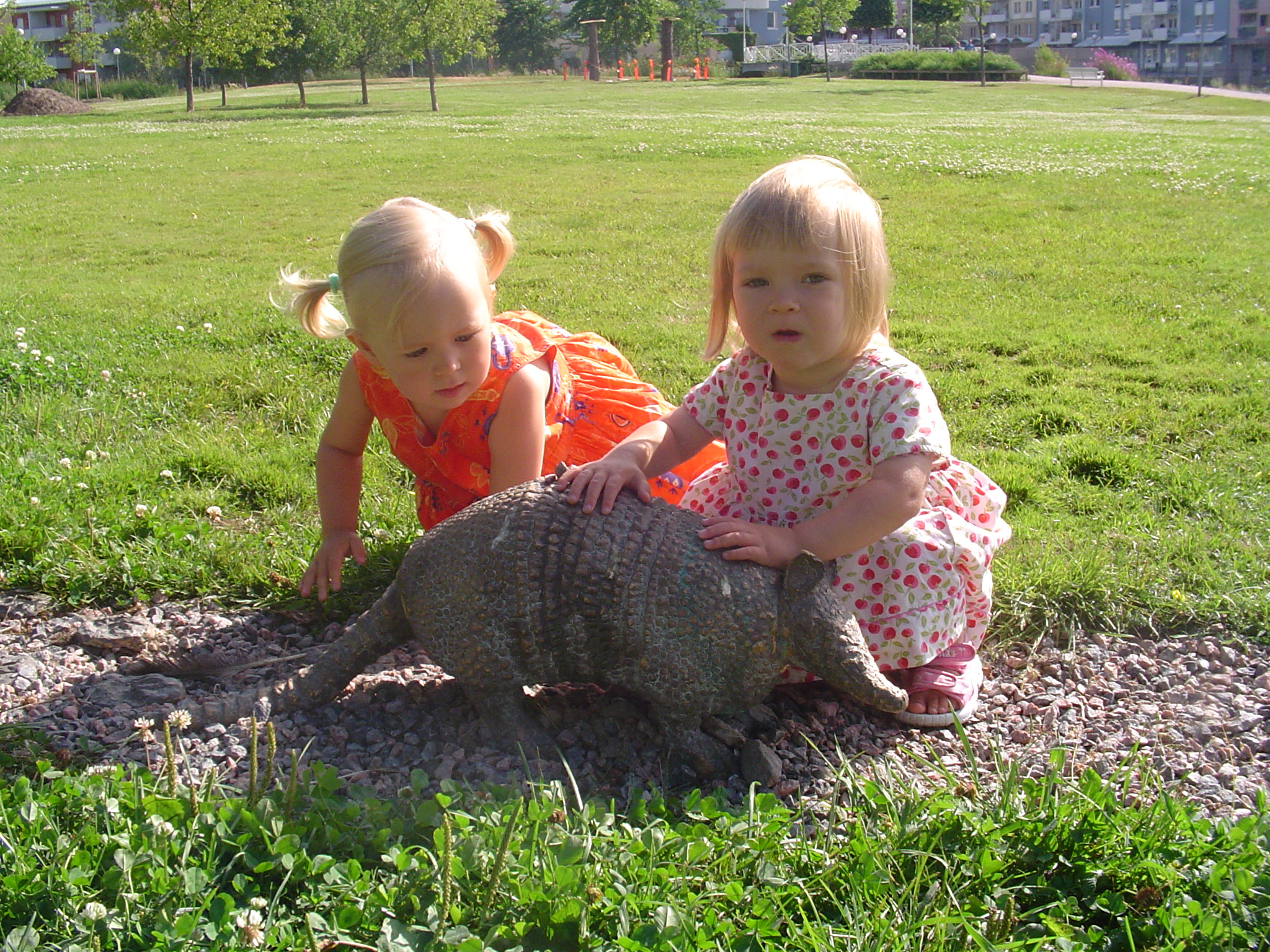 Public Artwork - Flower of Life - Two young children gently touching and exploring a bronze armadillo sculpture in a grassy park. - Art park, Pikku-Huopalahti, Helsinki, 2005.