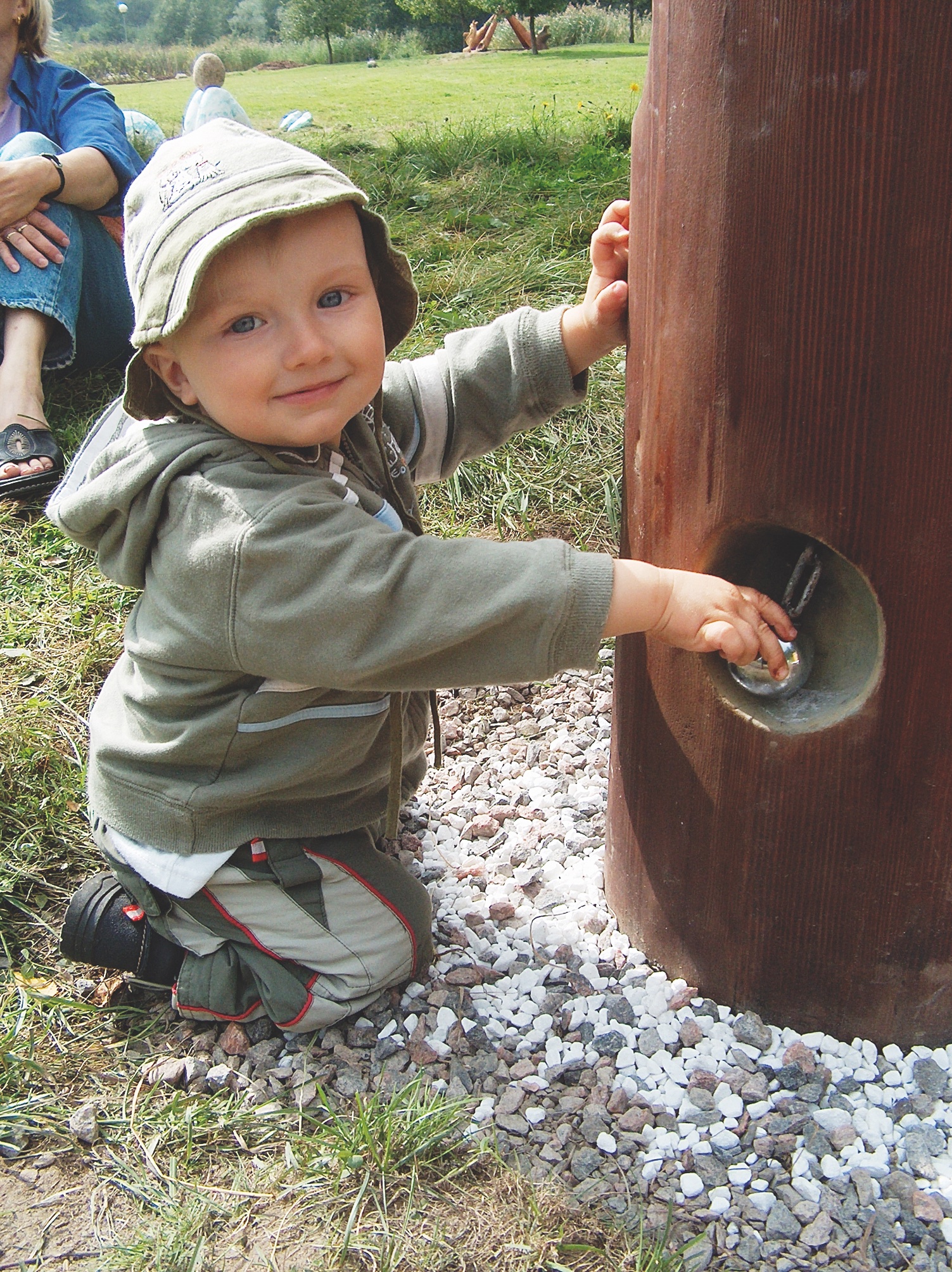 Public Artwork - Flower of Life - A child interacting with a wooden sculpture featuring a small reflective metal element. - Art park, Pikku-Huopalahti, Helsinki, 2005.