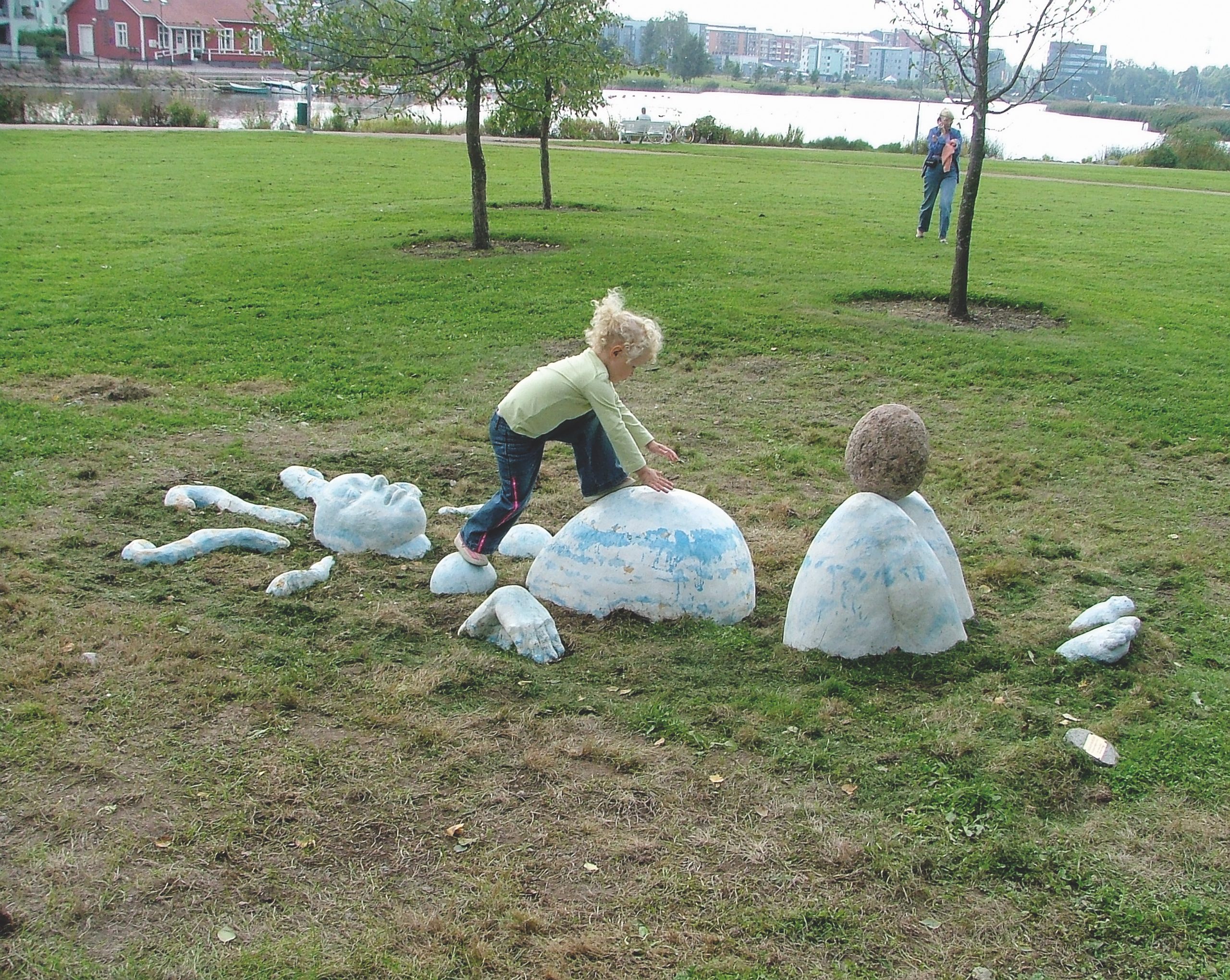 Public Artwork - Flower of Life - A child climbing among abstract sculptures resembling body parts and egg-shaped forms in a grassy park. - Art park, Pikku-Huopalahti, Helsinki, 2005.